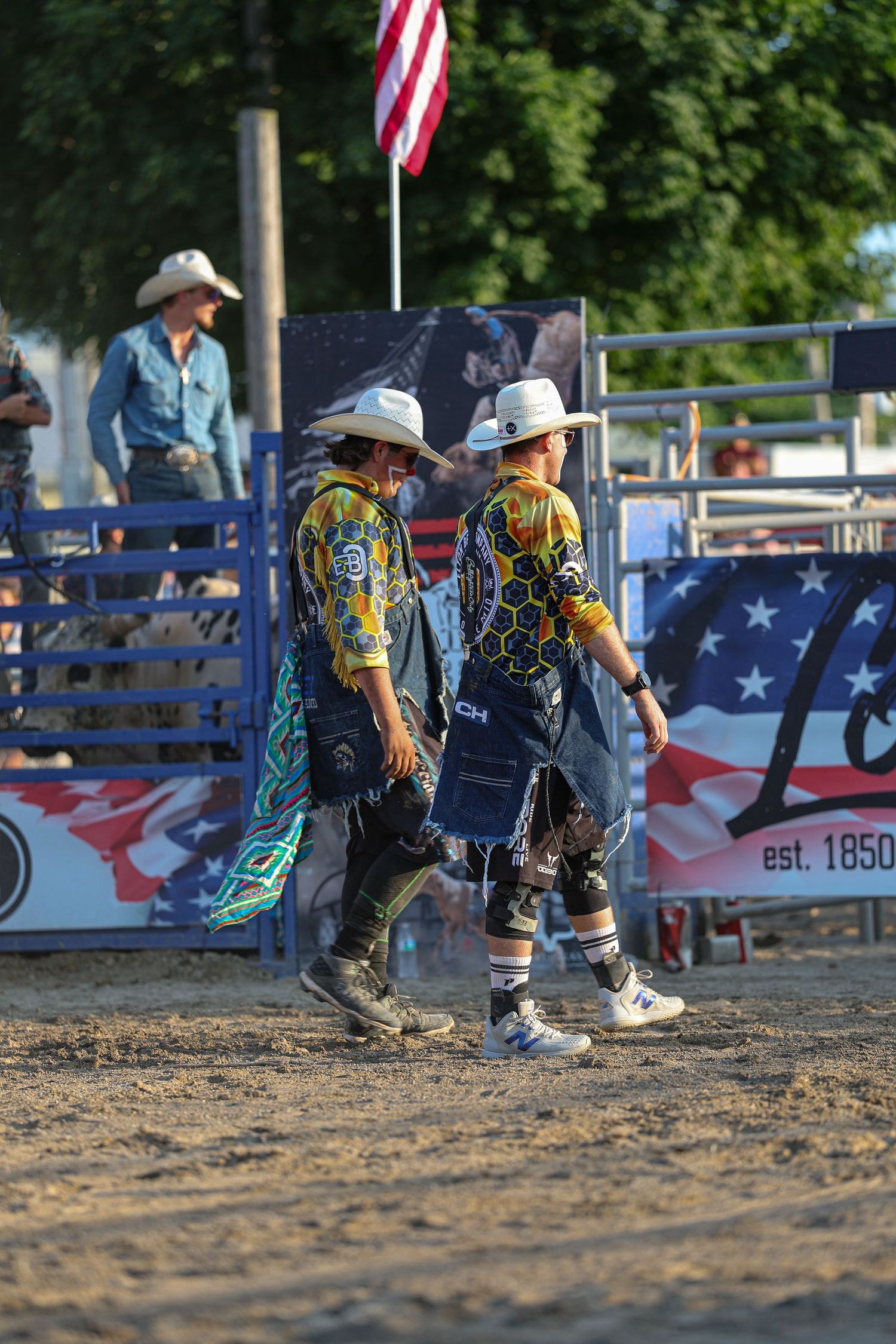 Two cowboys walking through the arena in front of the flag